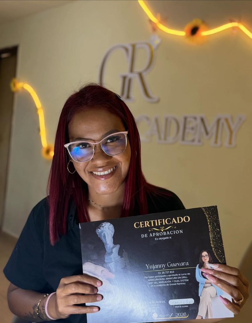 Alumna con su certificado frente al letrero de la academia